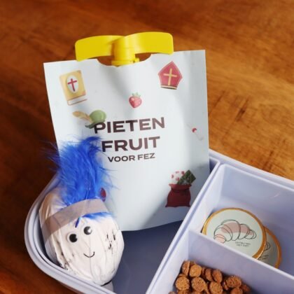 Een knijpfruitje in een blauwe broodtrommel met een gepersonaliseerde Sinterklaas knijpfruitwikkel